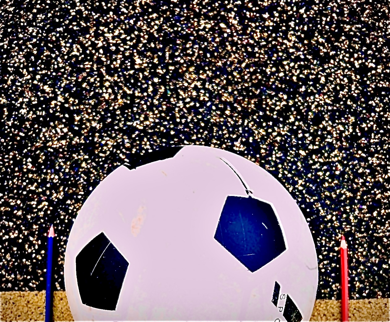 Balón de futbol en una cancha con un lápiz azul a la izquierda y uno rojo a la derecha.